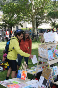 Deux cyclistes discutes à propos un livre pris sur le stand librairie dans le parc. Arrière plan d'un arbre. Premier plan du présentoire de livres.