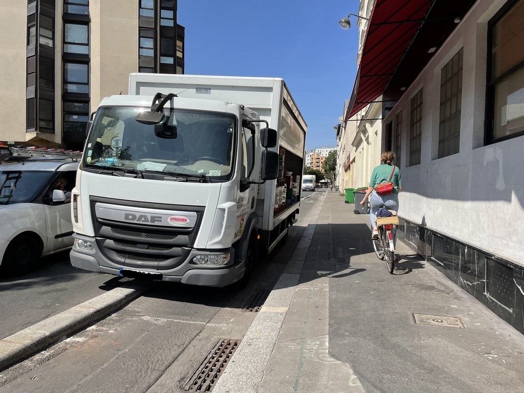 Un camion obstrue la piste cyclable, et la cycliste roule sur le trottoir. Paris, été 21.